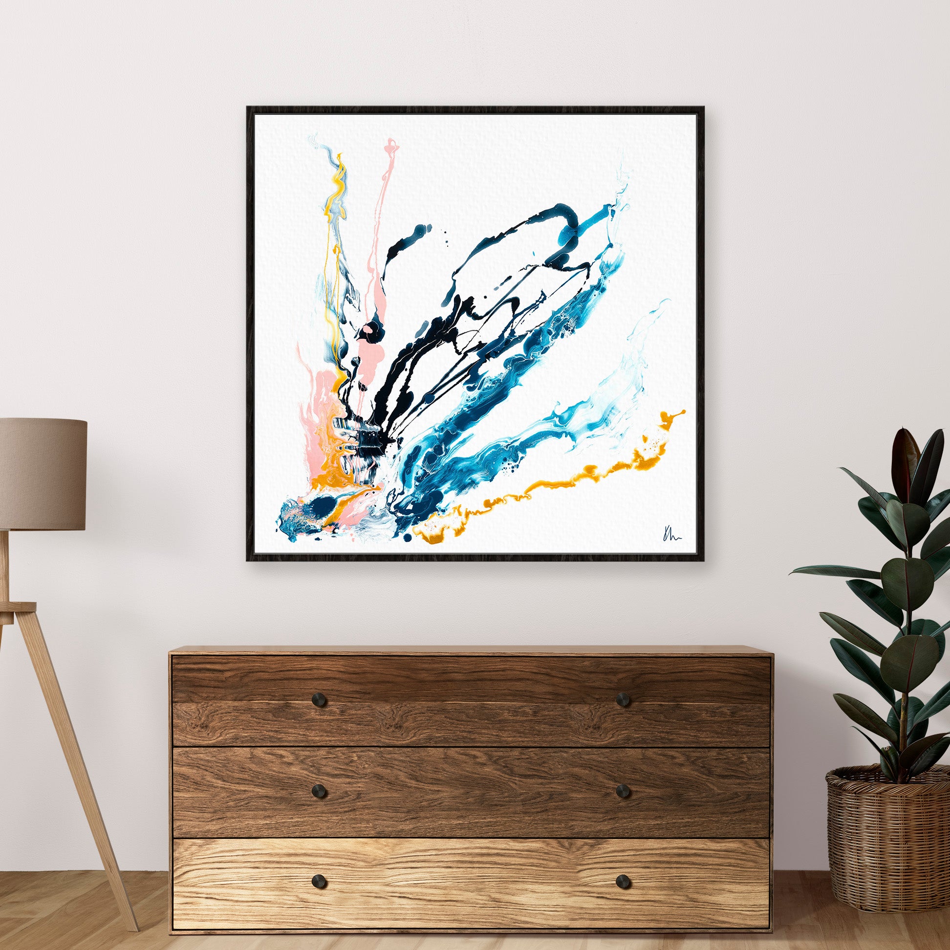 The wooden chest of drawers is adorned with "Then There Was You," an abstract painting by Kate Mayer featuring blue, yellow, and pink splashes. A lamp and plant sit beside it.