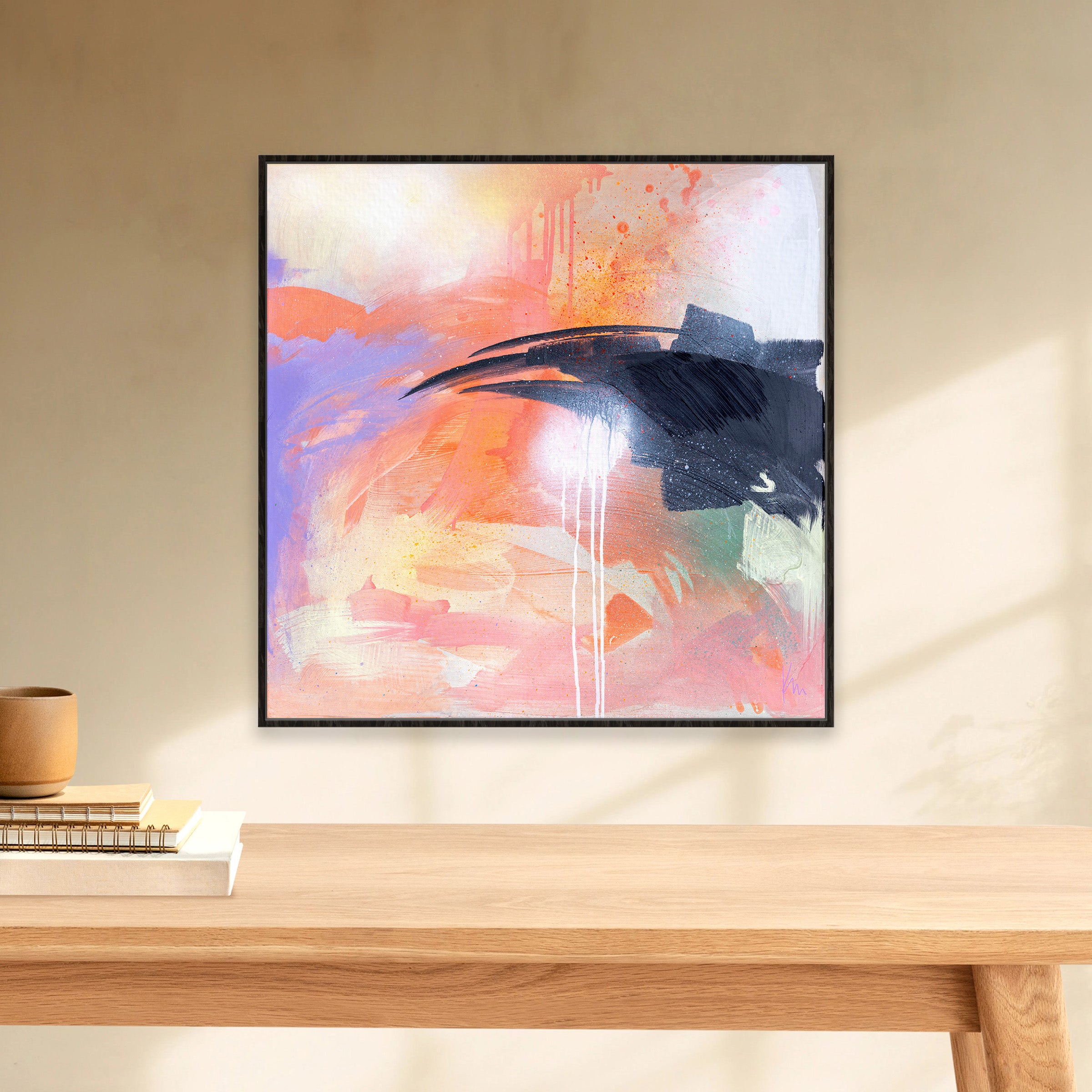 The "Beneath The Surface" abstract painting by Kate Mayer, featuring pink, orange, and blue hues, is displayed on a beige wall above a wooden shelf adorned with books and a small vase.