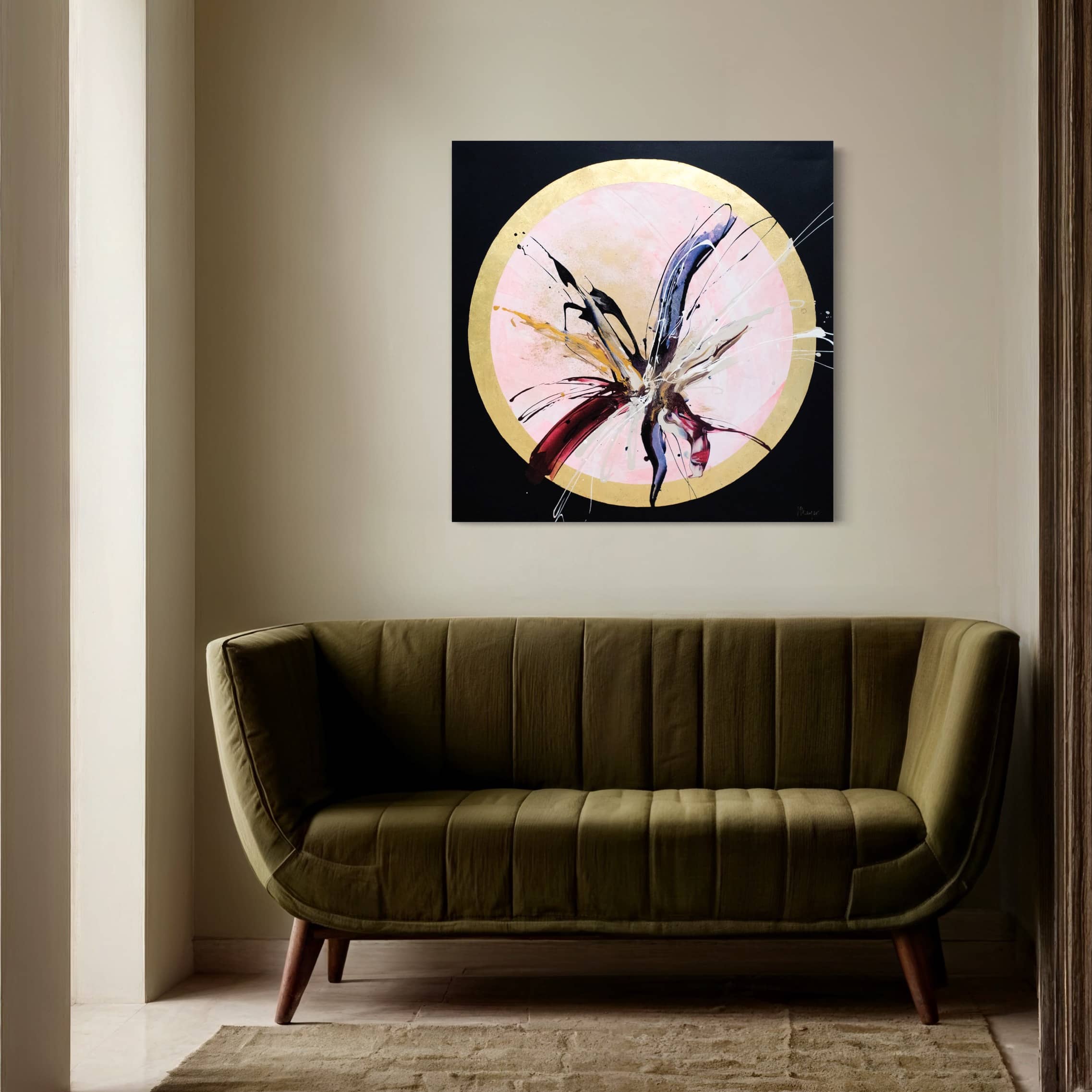 The "Innervisions" original painting by Kate Mayer, featuring abstract flower-like strokes accented with acrylic and gold leaf, elegantly hangs above an olive-green sofa in the minimalist room.