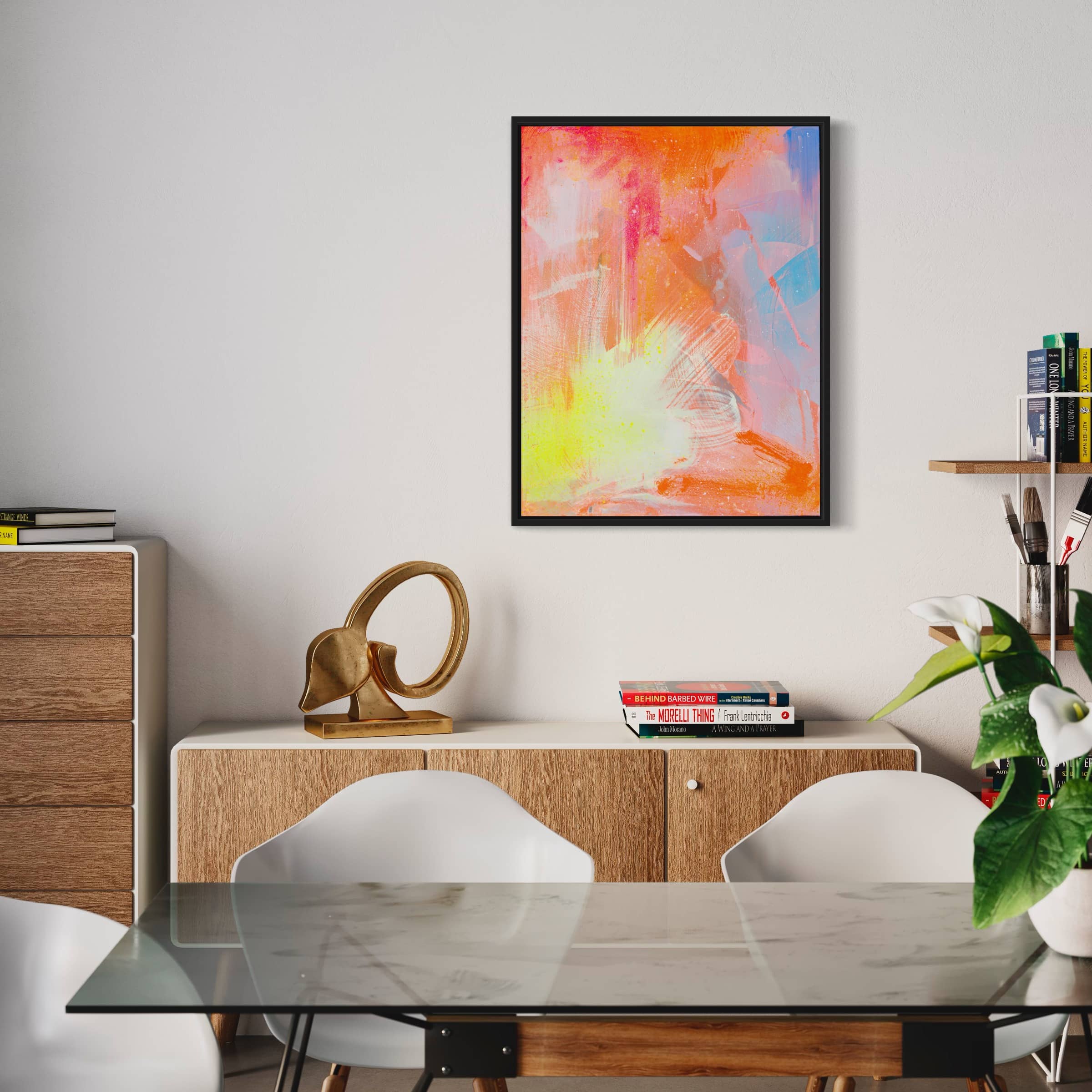 A modern dining room showcases a captivating painting, "Dream Big" by Kate Mayer, on the wall, highlighted with vibrant strokes of acrylic and spray paint. The space also includes a sleek wooden sideboard, curated books, and elegant white chairs around a glass table.