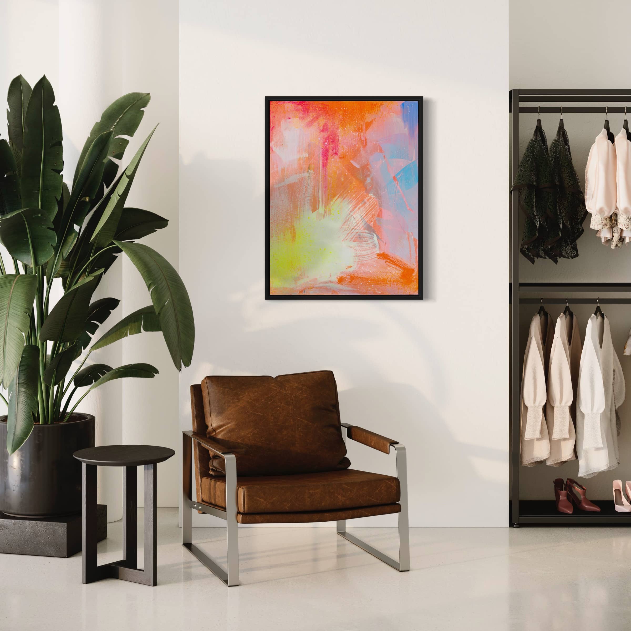 A stylish living space with a brown leather chair, the "Dream Big" original painting by Kate Mayer, crafted with acrylic and spray paint, a large plant, and a clothes rack.