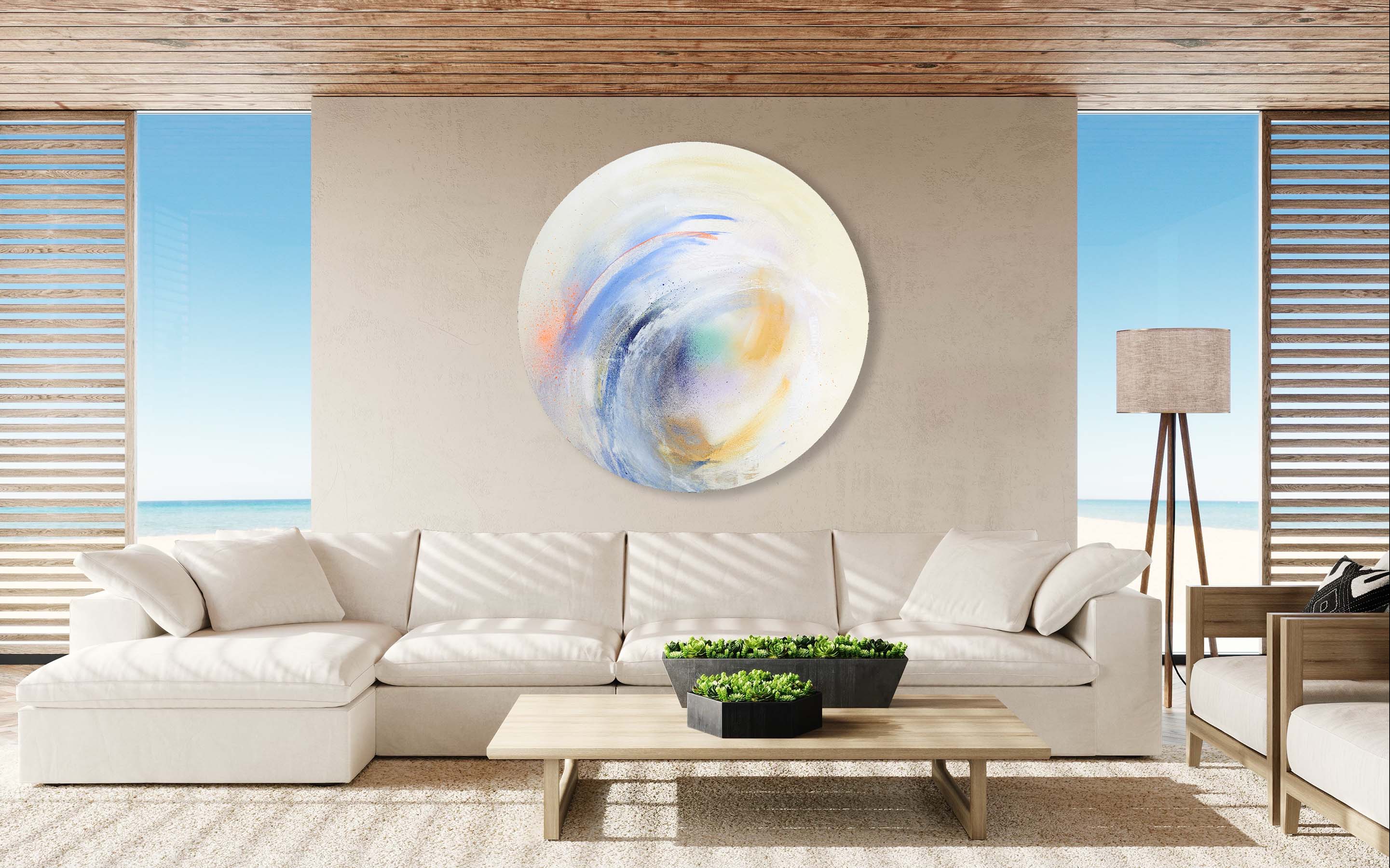 A modern living room showcasing a white sectional sofa, Kate Mayer's "Free Spirit" original painting in acrylic on canvas embellishing the wall, a coffee table adorned with plants, and an ocean view.