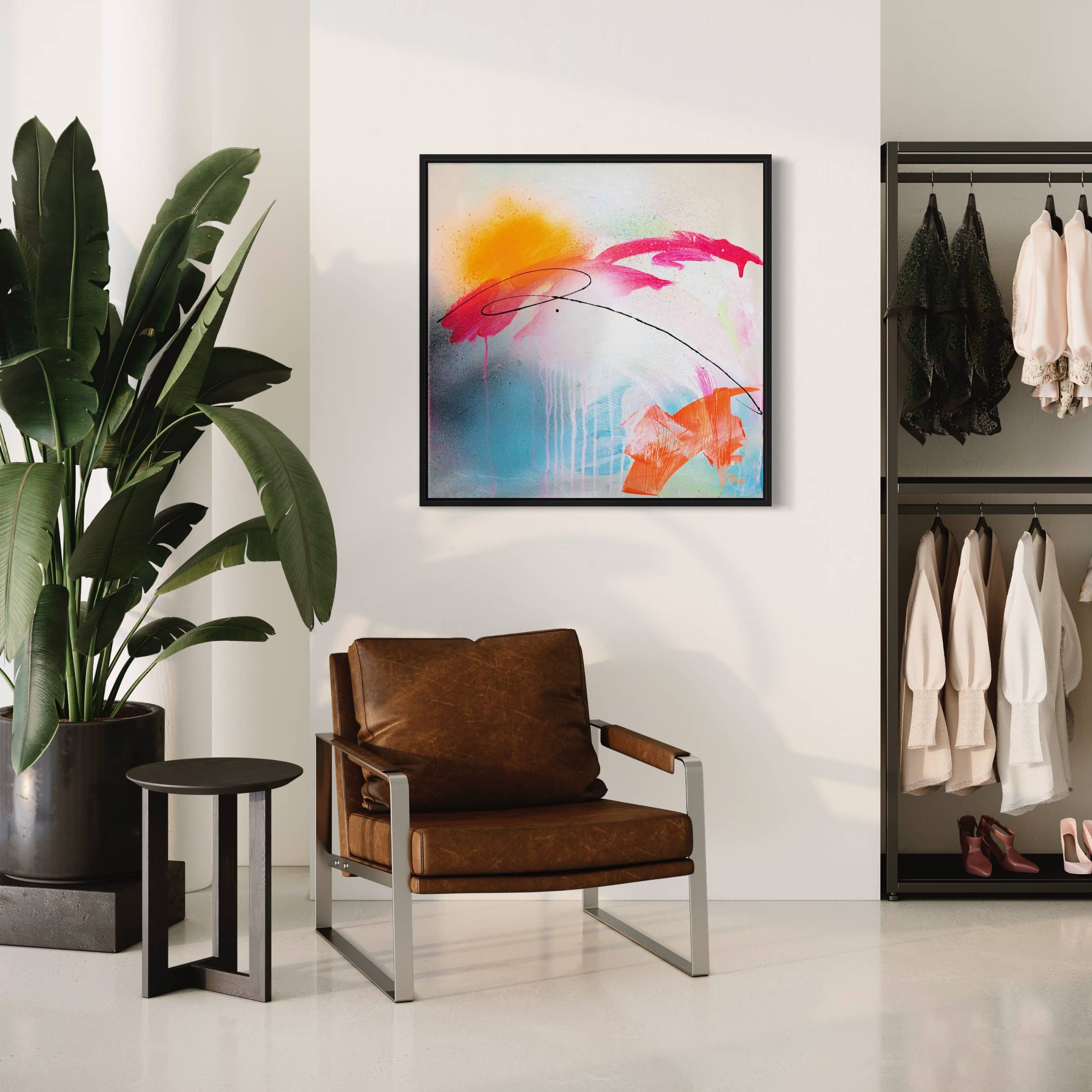 A modern room with a brown leather chair, a side table, a large plant, Rise & Shine Bright - Original Painting by Kate Mayer on the wall, and a clothing rack with hanging clothes.