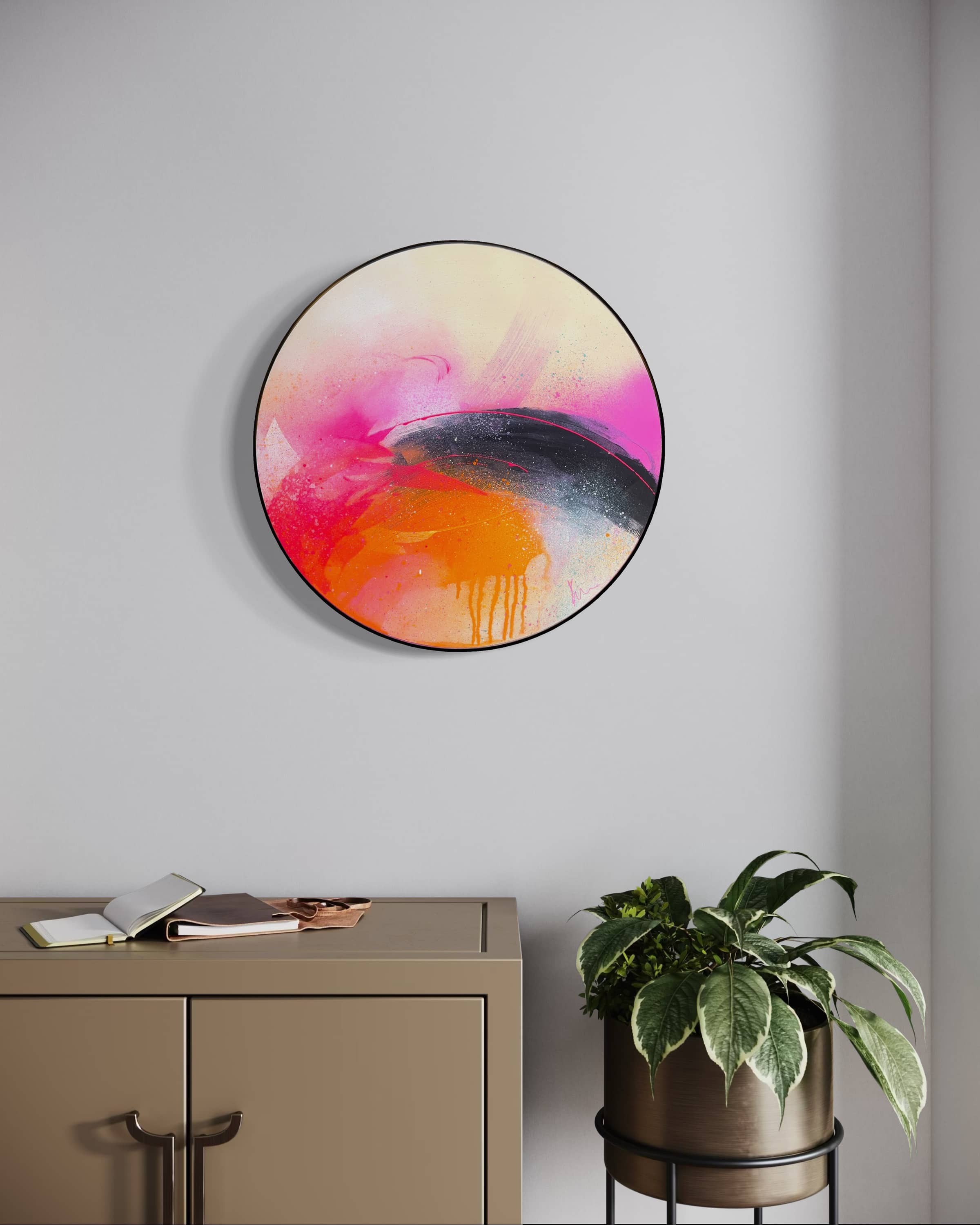 A modern room displays "I Carry On" by Kate Mayer—circular acrylic art above a cabinet and potted plant.