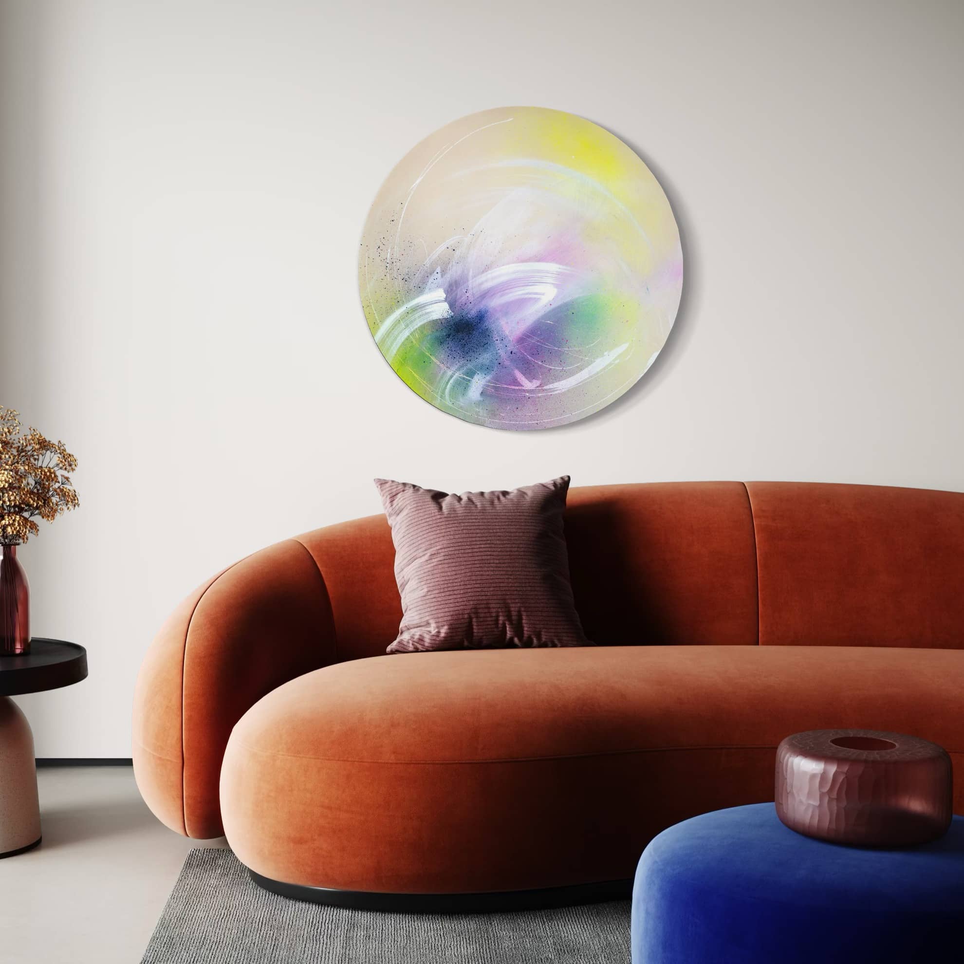 A modern living room with an orange sofa, Kate Mayer's "I Believe In Miracles" round painting, and a purple cushion.
