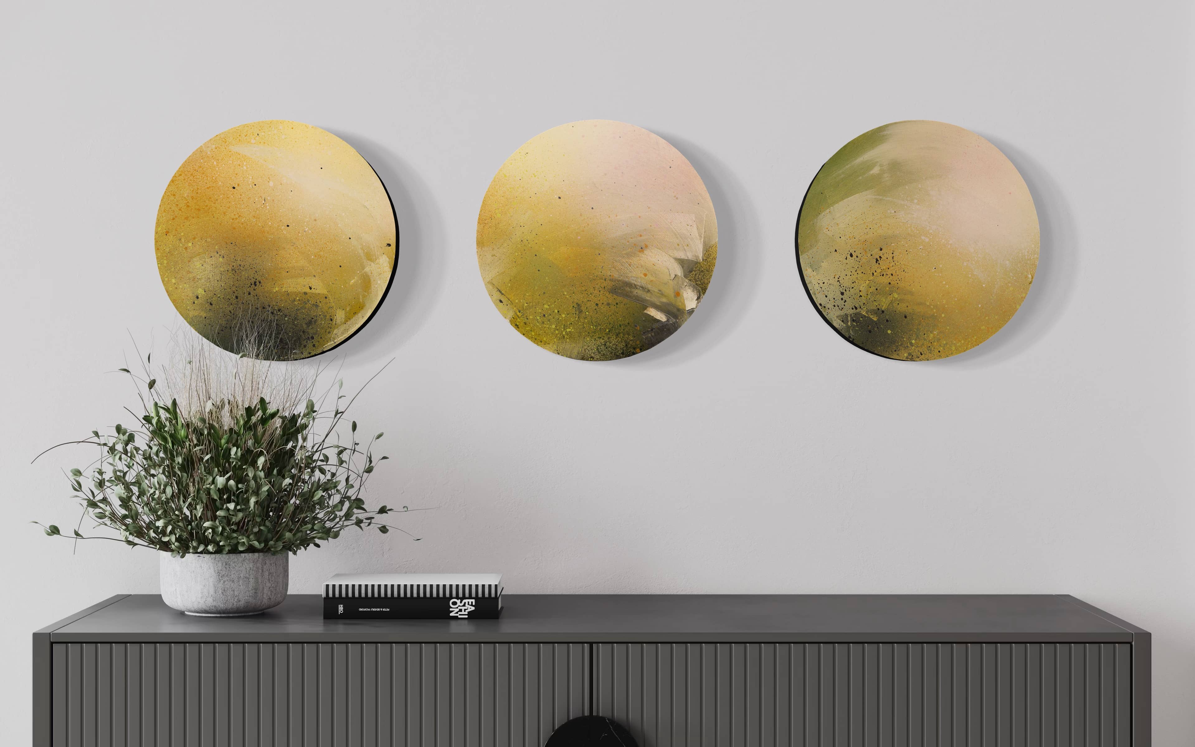 Three "Meadowlarks" round abstracts by Kate Mayer hang above a cabinet with a plant and closed notebook on top.