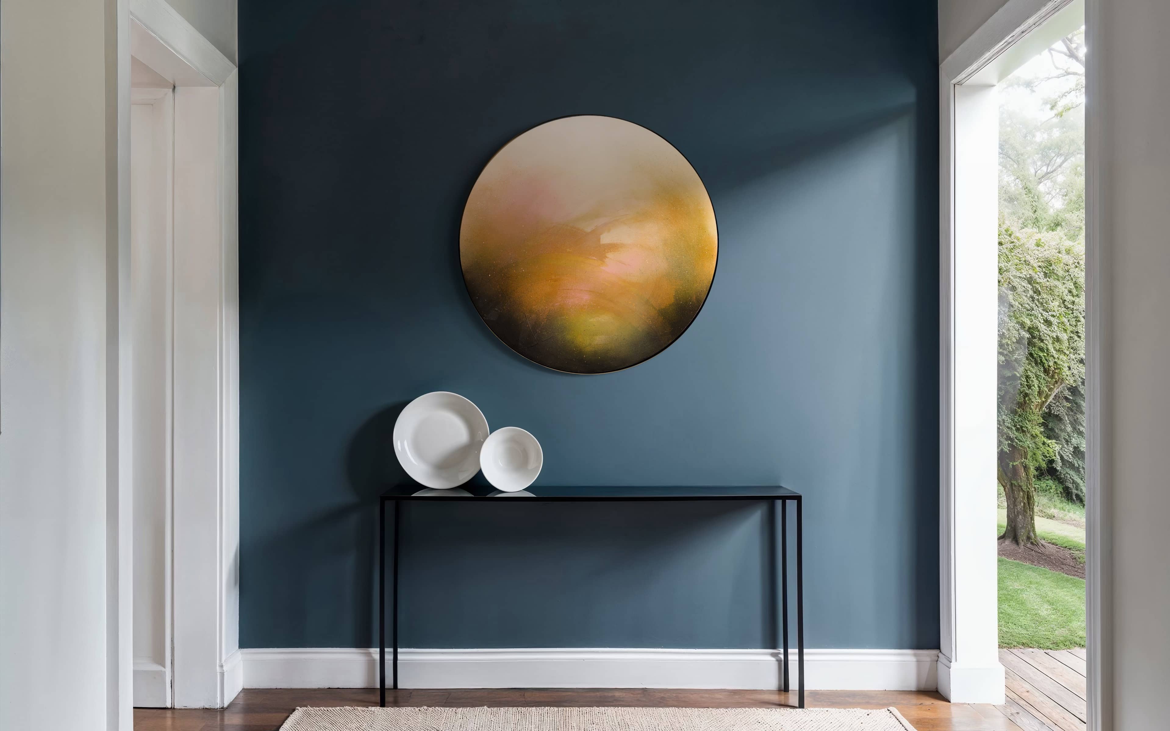 “Only Now I See The Light” by Kate Mayer, a round painting, hangs above a black console with three white bowls.