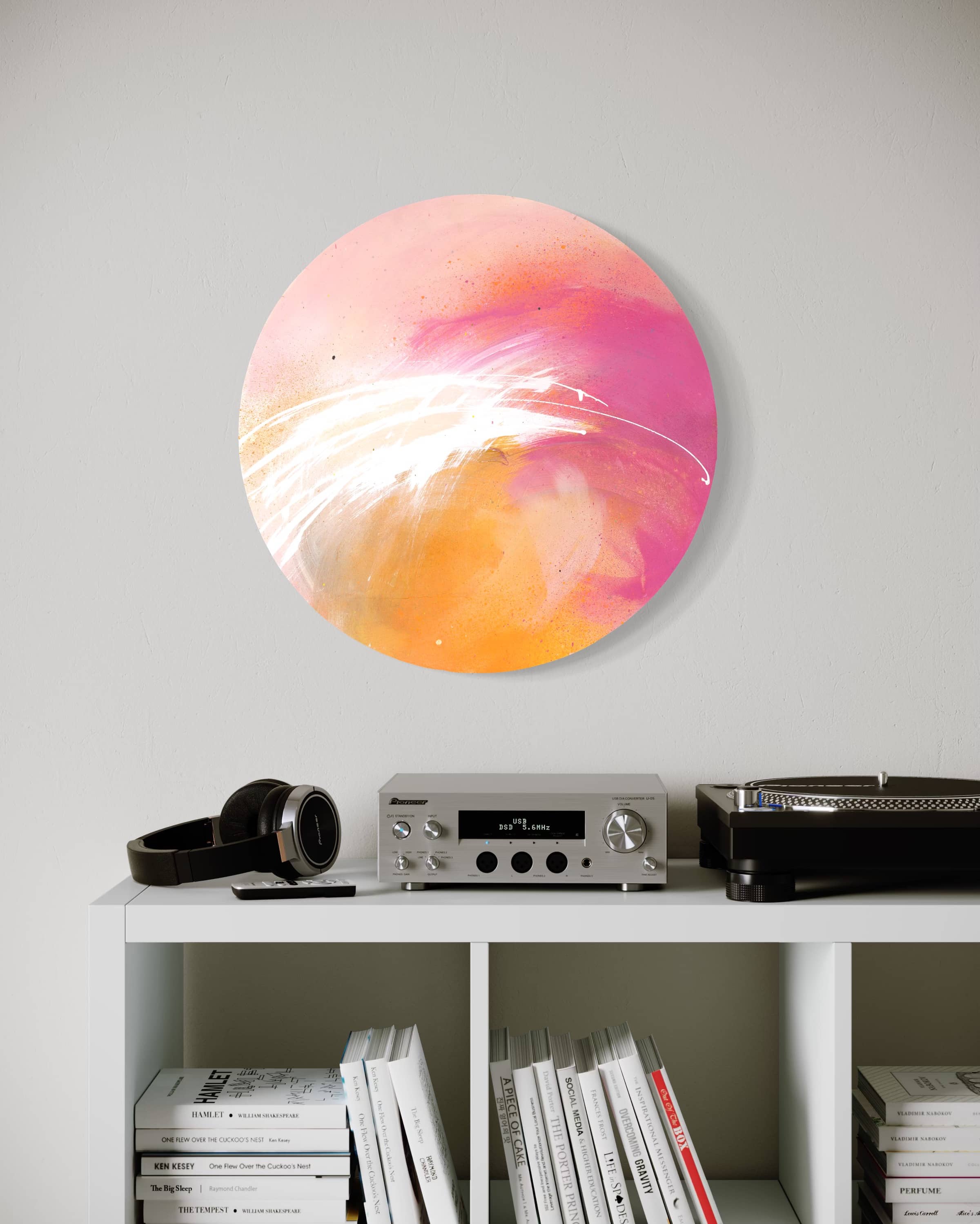 Shine On" by Kate Mayer, a round pink and orange abstract on plywood, hangs above a stereo and books.