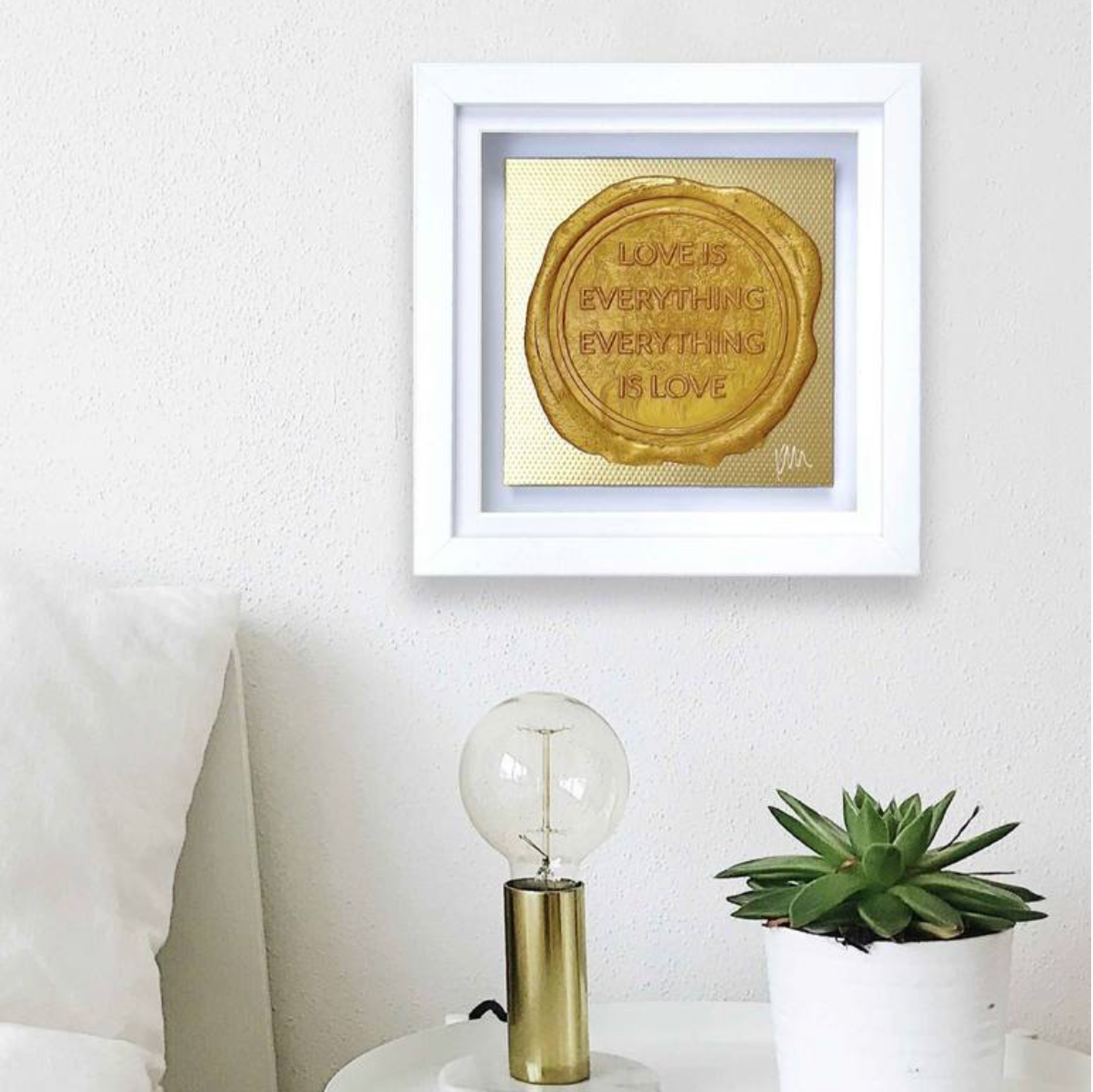 Framed original "Sealed Intention for LOVE" by Kate Mayer with the quote "Love is everything, everything is love" above a lightbulb lamp and potted succulent on a white table. Includes a certificate of authentication.