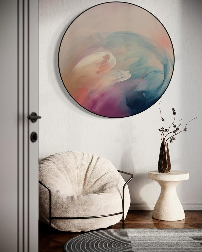 Cozy armchair, round table, vase with twigs, and “For Every Mountain” by Kate Mayer framed on the wall.