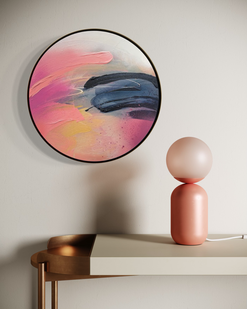 Looking For You“ by Kate Mayer, a round acrylic painting in pink, orange & blue, hangs above a modern console lamp.