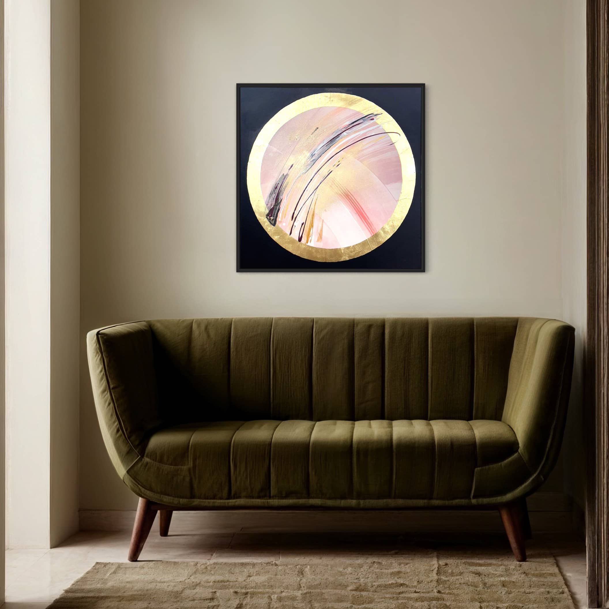 A modern green sofa sits against a beige wall beneath "Fly With Me" by Kate Mayer in a black frame, featuring a circular design with acrylic and gold leaf accents.