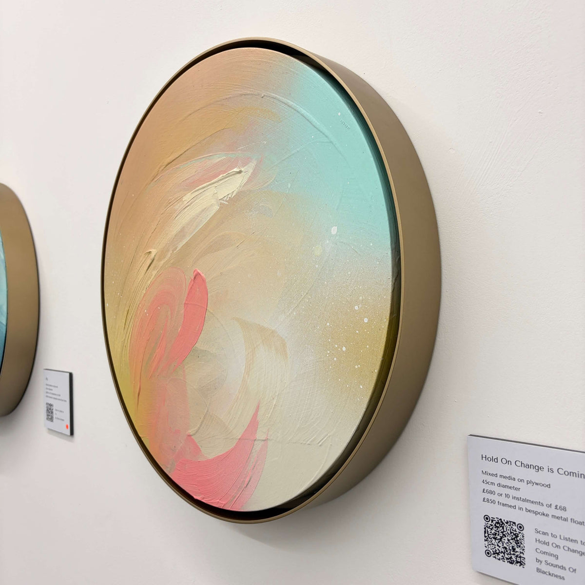 Hold On Change Is Coming“ by Kate Mayer: round pastel art in a handmade metal float frame on a white wall.